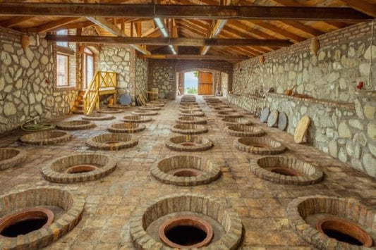 Georgian wine cellar with rows of traditional qvevri vessels set into the ground, surrounded by stone walls and wooden beams.