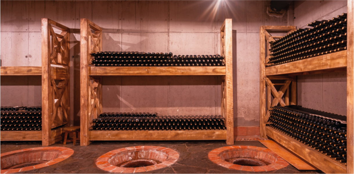 Wine bottles stored on wooden shelves in a cellar with qvevri at Giuaani winery