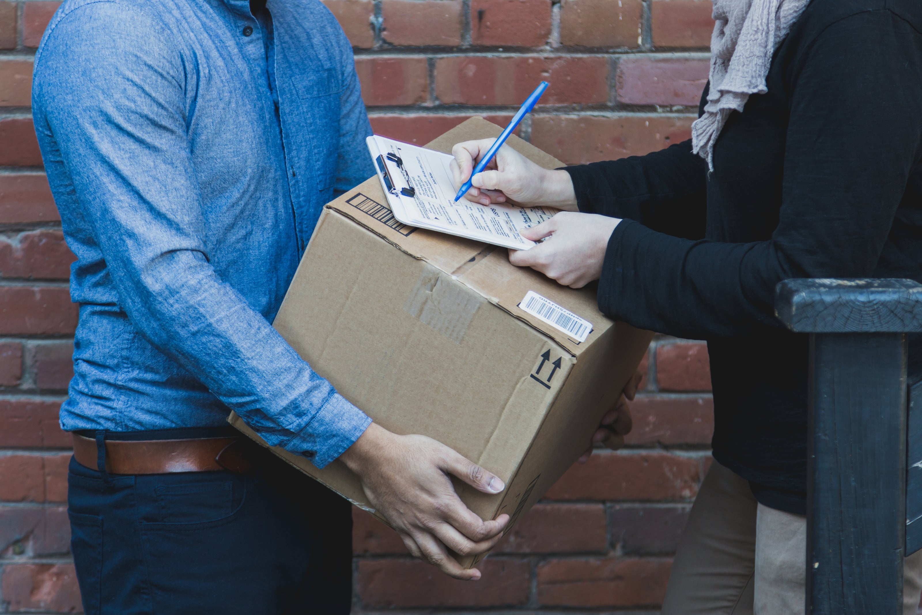 Man signing for a shipping box delivery against a brick wall background